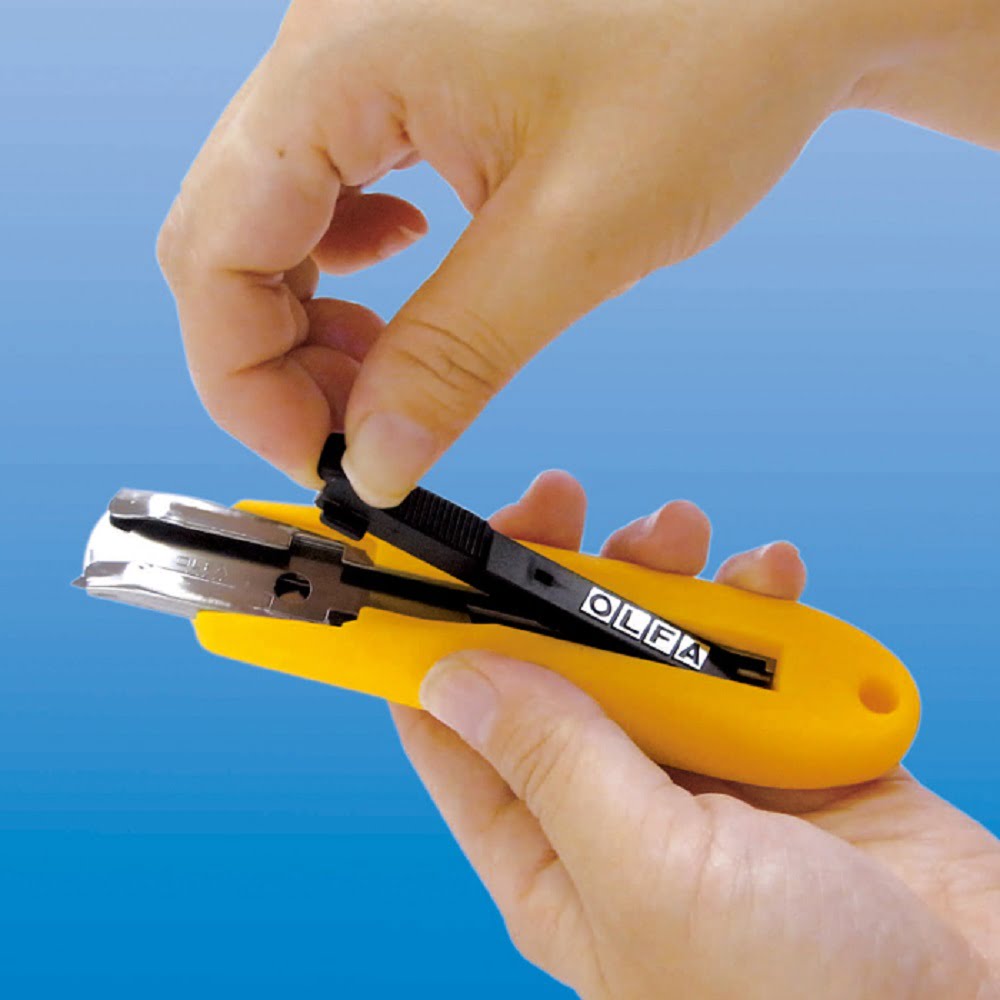 doua maini care desfac un cutter galben cu lama prevazuta cu arc pentru siguranta