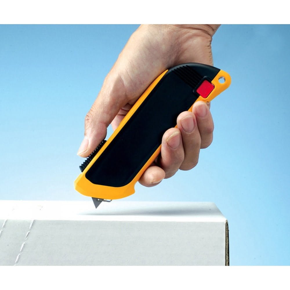 mana cu un cutter galben cu negru cu lama ascunsa si o cutie de carton