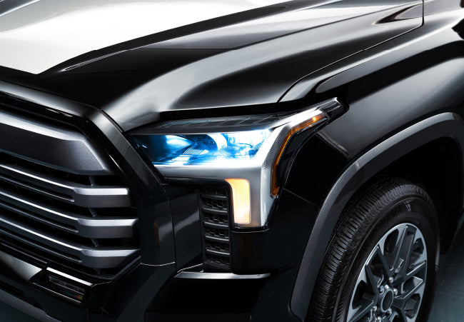 Prim-plan al farului frontal al unui SUV negru si al designului grilei cu lumini LED albastre luminate.