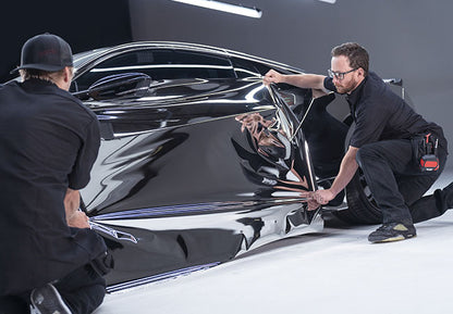 doi barbati care aplica o folie auto argintie lucioasa pe lateralul unei masini