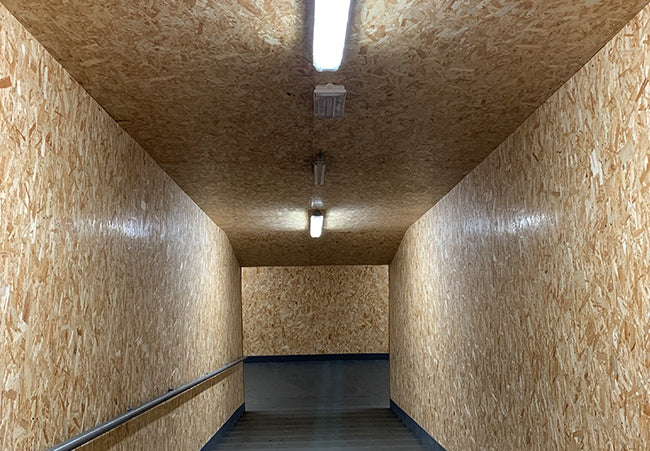 Interiorul unui coridor ingust cu pereti si tavan din placi PFL, cu o scara luminata de neoane fluorescente.